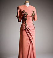 A pink dress on a mannequin, it's a coral color with gold designs on the sides